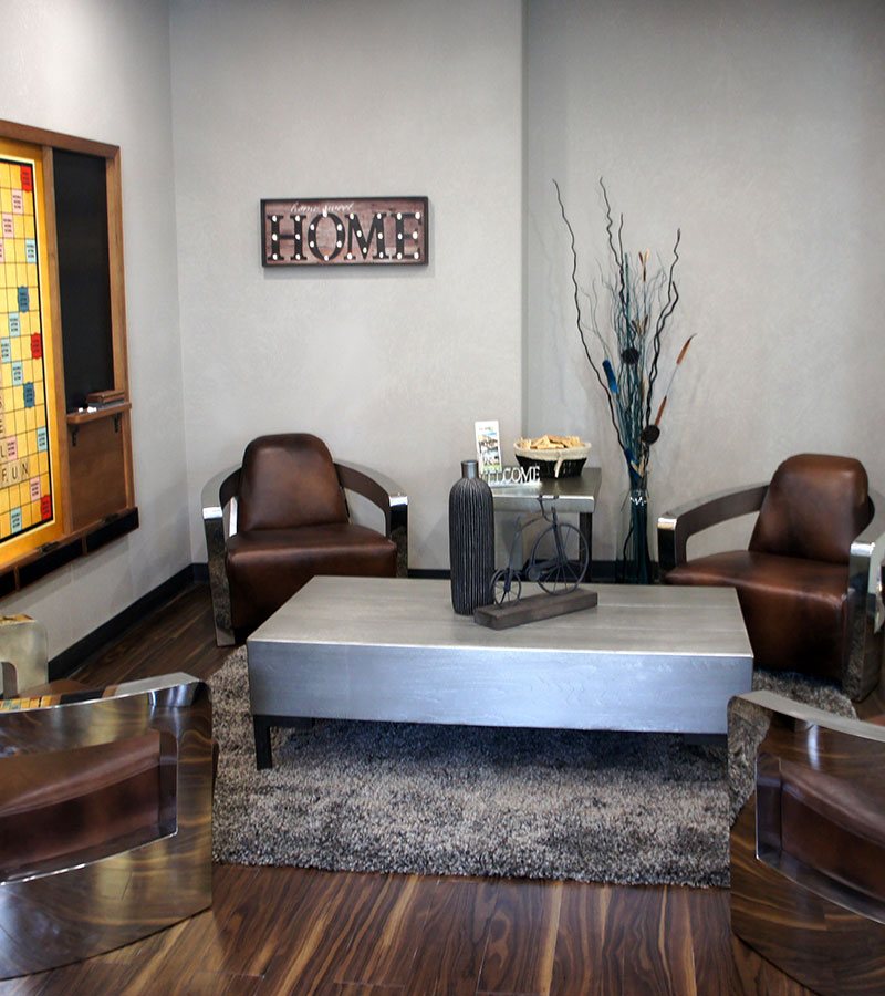 Four chocolate brown leather lounge chairs are placed around a heavy steel top coffee table embellished with decorative knick-knacks in the lounging area at the d3h Home Inn Express by d3h™ Medicine Hat hotel in Alberta.